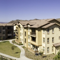 Tan three story apartment buildings with garage and reddish-beige roof and mountains in the background