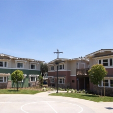 Angled view of apartment homes with a street light and electrical pole to the right and a half basketball court to the left