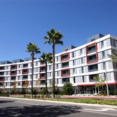 Grey, white, and red apartment building with three palm trees in front