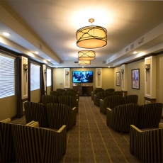 Small movie theatre with two rows of coupled chairs and hung lighting fixtures