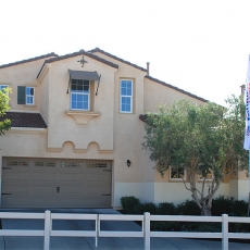 Tan two story house with windows and garage door with a fence in front
